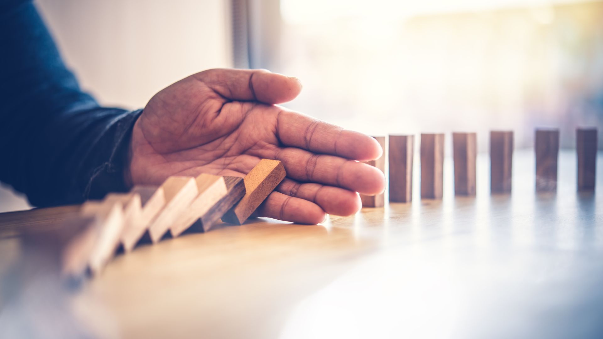 Hand stoppt fallende Dominosteine, symbolisiert Stabilität durch breit diversifizierte Anlagestrategien statt kurzfristiger Spekulation.